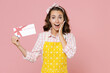 © ViDi Studio - Excited young brunette woman housewife 20s wearing yellow apron hold gift certificate put hand on cheek while doing housework isolated on pastel pink background studio portrait. Housekeeping concept.