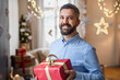 © Halfpoint - Mature man indoors at home at Christmas, holding present.