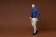 © ViDi Studio - Full length side view of smiling successful young business man wearing blue shirt tie looking aside isolated on brown colour background studio portrait. Achievement career wealth business concept.