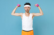 Confused young strong sporty fitness man with thin skinny body sportsman in white headband shirt shorts doing exercise with dumbbells isolated on blue background. Workout gym sport motivation concept.