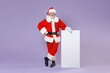 © ViDi Studio - Full length portrait of smiling Santa Claus man in Christmas hat red suit coat glasses hold big white empty blank billboard isolated on violet background. Happy New Year celebration holiday concept.