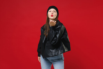 Wall Mural - Beautiful attractive pretty young brunette woman wearing casual black leather jacket white t-shirt hat blowing sending air kiss looking camera isolated on bright red colour background studio portrait.