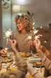 © Seventyfour - Vertical portrait of carefree mixed-race woman holding sparklers while enjoying dinner party and celebration with friends and family