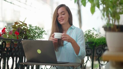 Wall Mural - Beautiful happy cute joyful smiling romantic woman blogger drinking an aromatic coffee while working online at a laptop on a balcony