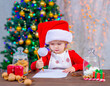 Little cute girl in santa hat writes a letter to Satna Klaus