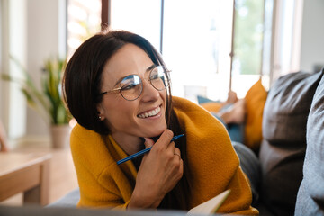 Wall Mural - Beautiful woman smiling and writing in notebook on sofa in apartment