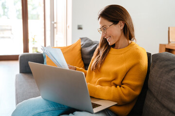 Beautiful caucasian woman working with laptop and papers in apartment