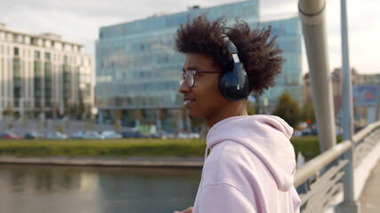 Wall Mural - Young handsome african american man listening to music using headphones standing on city bridge