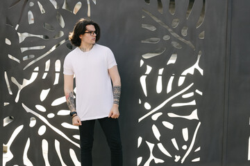 Wall Mural - Hipster handsome male model with glasses wearing white blank t-shirt and black jeans with space for your logo or design in casual urban style