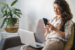 © Tijana - Smiling woman using mobile phone and laptop computer at home stock photo