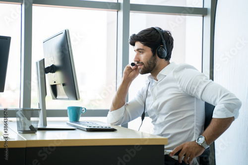 Smiling handsome young male call centre operator with headset.Confident male customer service representative,operator,agent,call centre worker,support staff speaking with head set in modern office