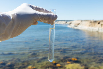 Sample water from the baltic sea for analysis. Hand in white glove holding a test tube.
