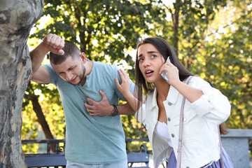 Canvas Print - Woman calling ambulance to help man with heart attack in park