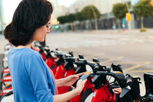 Woman Consulting Phone In A Bike Rental Station