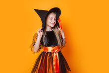 Cute Little Girl In Witch Halloween Costume On Orange Background
