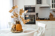 © Юлия Клюева - Branches with Golden leaves and a pumpkin on a tray. In the background-the interior of a white kitchen in the Scandinavian style. The concept of home comfort. Autumn decor for the Halloween holiday.
