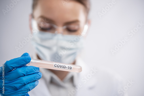 Close-up view of doctor in mask and protective blue gloves keeps covid-19 vaccine on white background. Scientific discovery. Healthcare and coronavirus infection concept.