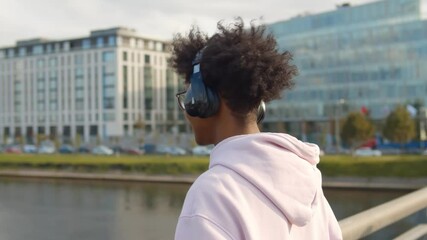 Wall Mural - Young handsome african american man listening to music using headphones standing on city bridge