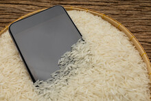 A Wet Smartphone Is Dried In Rice On Wooden Background
