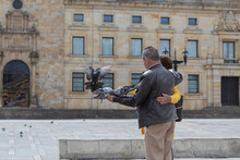An Old Couple Feeding Pigeons Possing For A Photo At Bogota Bolivar Square Downtown With Colonial Building Behind Them. 