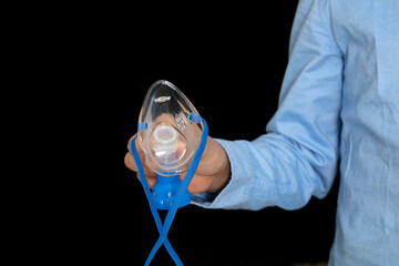 Close-up of hand holding nebulizer inhalation hood in front of black background