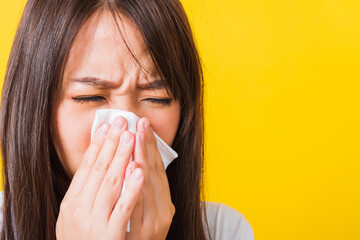 Wall Mural - Portrait of Asian beautiful young woman sad she crying wipe the mucus with tissue, Close up of pretty girl sneezing sinus using towel to wipe snot from nose, studio shot isolated on yellow background