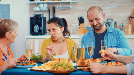 Extended family interacting while having a meal at dining table in the kitchen. Multi generation, four people, two happy couples talking and eating during a gourmet dinner, enjoying time at home.