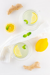 Wall Mural - Ginger tea with lemon and mint on a white napkin. Two cups of ginger tea, lemon, ginger root and honey on white background. Top view