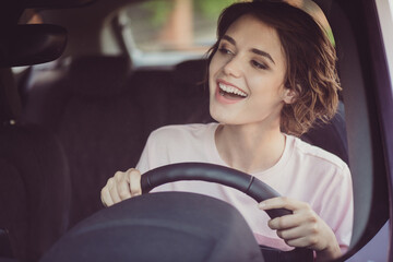 Wall Mural - Photo of lovely pretty lady beaming shiny smiling positive cheerful face hold steering wheel drive car look road see neighbor signaling beeping him greeting wear white shirt indoors