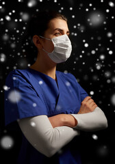 Poster - health, medicine and pandemic concept - young female doctor or nurse wearing face protective mask for protection from virus disease over snow on black background in winter