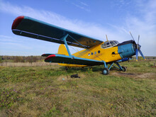 Yellow And Blue Old Biplane Plane With A Single Piston Engine And Propeller Against A Blue Sky With Clouds On The Airfield With Green Grass In Summer