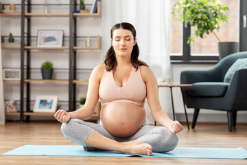 Wall Mural - sport, yoga and people concept - happy pregnant woman with earphones and smartphone listening to music and meditating at home