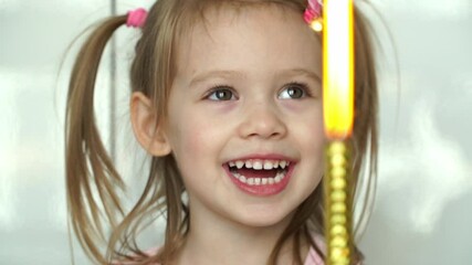 portrait of little smiling girl blows out birthday candle in festive cake with fruits. close up of h