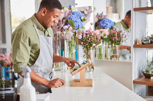 Joyful young man working as cashier at florist