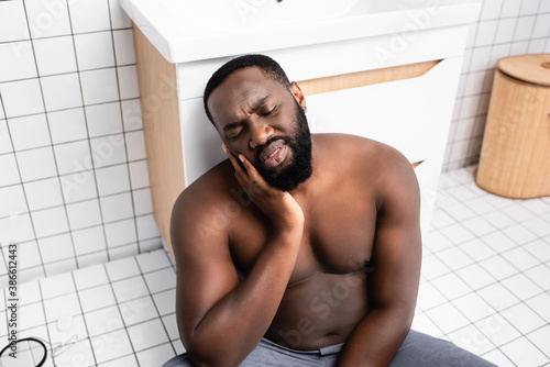 Fotomural afro-american man sitting on bathroom floor and grimacing from toothache