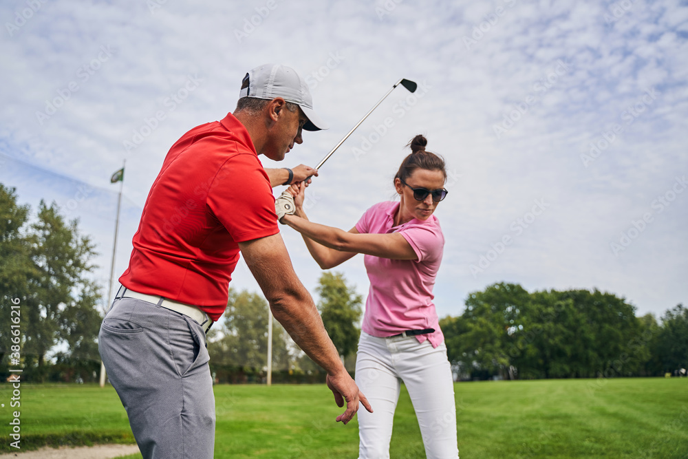 Golfer mastering a swing technique assisted by her coach - obrazy, fototapety, plakaty 