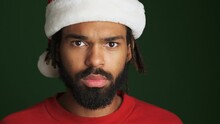 Young Serious African Man In Christmas Santa Hat Isolated Over Green Wall Background