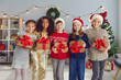 © Studio Romantic - Happy diverse children holding Christmas presents and looking at camera standing in cozy living-room