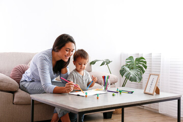 Young beautiful woman teaching her two year old son to draw at home. Woman spending quality time with her toddler child. Close up, copy space, background.