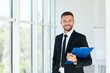 © GVS - Handsome smiling businessman with clipboard in a bright modern office