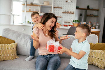 Two young sons are giving their mother a gift. Mother is suprised to receive a present from sons.