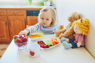 Wall Mural - Adorable toddler girl eating fresh fruits and vegetables for lunch