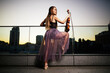 © Naz - A beautiful adult woman with long hair posing with violin on pointe shoes outdoors in city.
