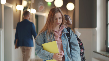 Beautiful upset woman student walking with books and backpack indoors