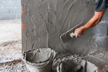 Closeup Hand Of Worker Plastering Cement At Wall In Construction Site