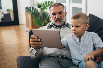 Canvas Print - grandfather with his grandson sitting on sofa and using tablet computer at home