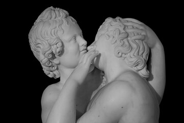 Couple of young statue are kissing, isolated on black background. Kiss marble ancient sculpture