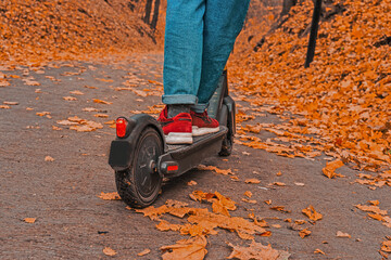 Cropped on woman legs feet riding on electric kick scooter in park. Electric transportation concept image. 