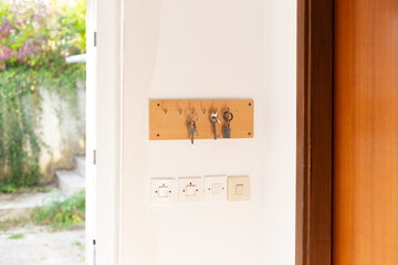 Wooden key holder on bright wall by the open main door of house