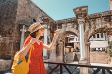 Traveler With A Toy Plane On The Background Of The Archaeological Monument - The Gate Of The Emperor Hadrian In The Old City Of Antalya. Concept Of Air Tickets And Airlines In Turkey